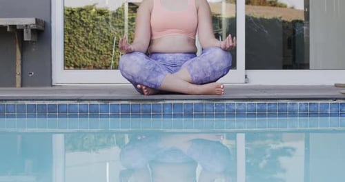 Konzentrierte biraciale Frau, die Yoga praktiziert und in Zeitlupe am Pool im Garten meditiert