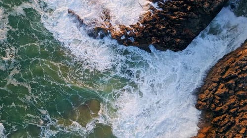 Rough ocean waves crashing on seashore stones black cliff top drone view