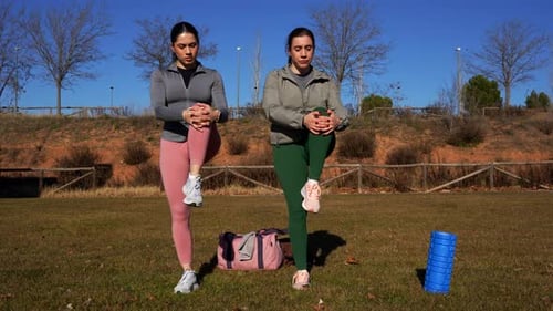 Two sisters doing leg and arm stretches in the park after running