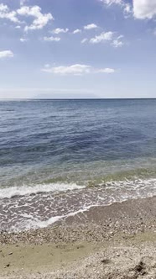 Relaxing seaside view of small waves rolling onto a sandy beach with seashells and footprints,