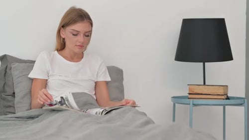Young Woman Reading Book while Sitting in Bed