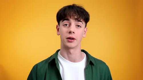 Young man talking while looking at the camera on a yellow background