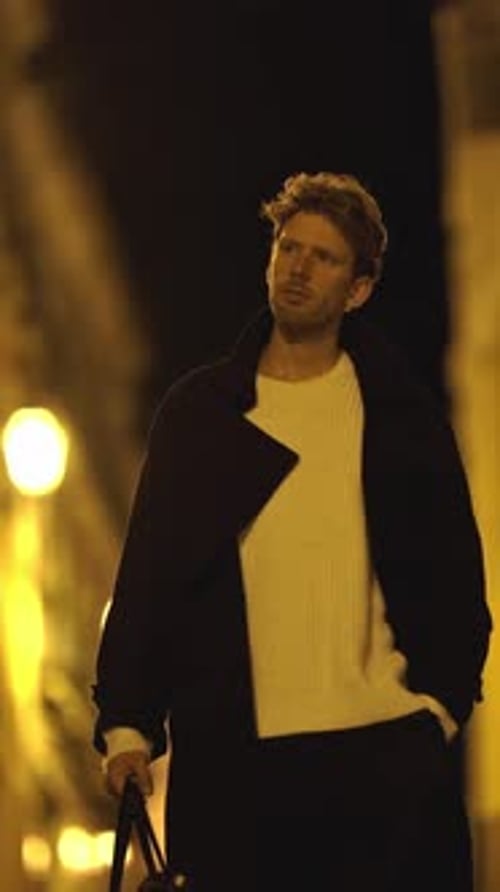 A Man is Walking Down a Street at Night Carrying