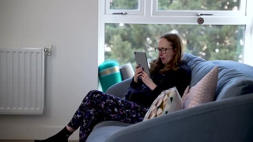Woman Using Tablet While Sitting on Couch at Home