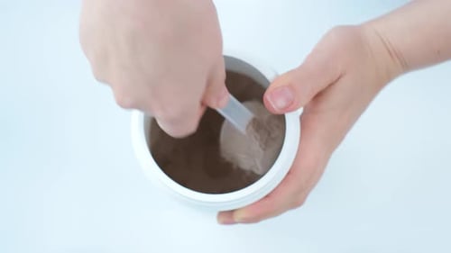 Chocolate protein powder in scoop and plastic jar on white background, top view.