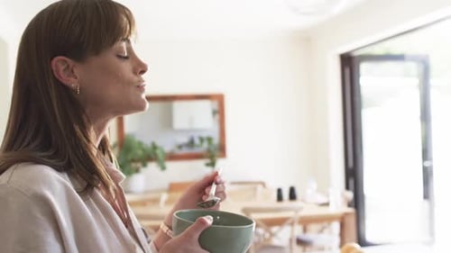Woman Eats Fruit for Breakfast in Bright Kitchen