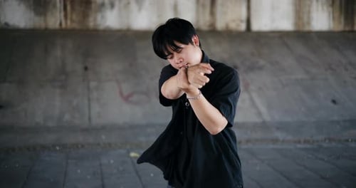 A stylish young man performs a freestyle dance under a footbridge in the city.