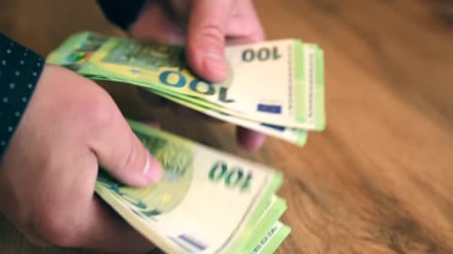 Hand holds out a pack of 100 euro bills but does not give it away close up, struggle for money