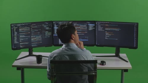Asian Man Thinking About Something While Write Code With Multiple Computer Screens In Green Screen