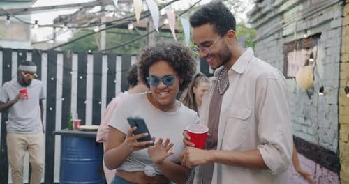 Young Adults Looking at Cell Phone at Outdoor Party