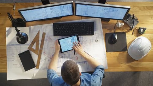 Top View of architectural Engineer Draws on His Blueprints, Compares with Tablet Computer with Gree