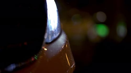 Closeup of rain hitting a cars front light in the night. City lights and traffic in the blurry backg