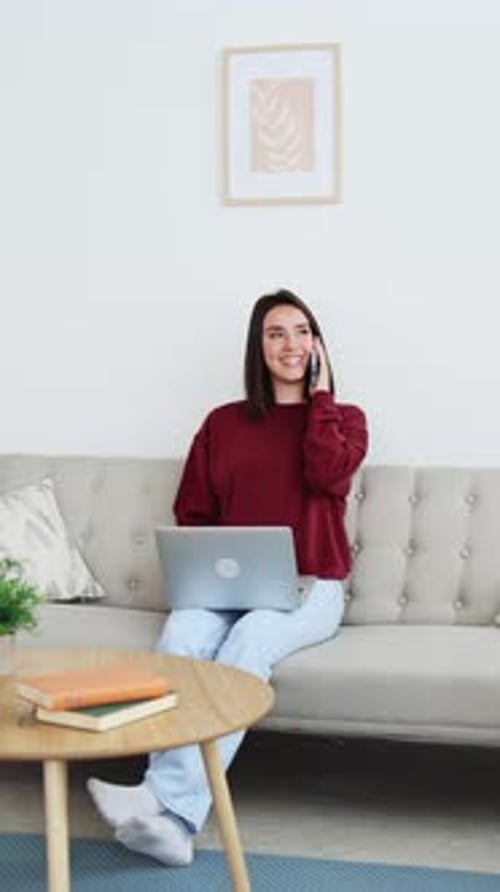 Woman Using Laptop and Talking on Smartphone at Home