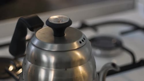 Boiling kettle on kitchen stove steam escaping through kettle holes