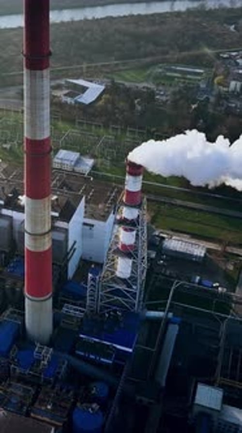 Tall smokestacks release steam above a power plant in a green landscape