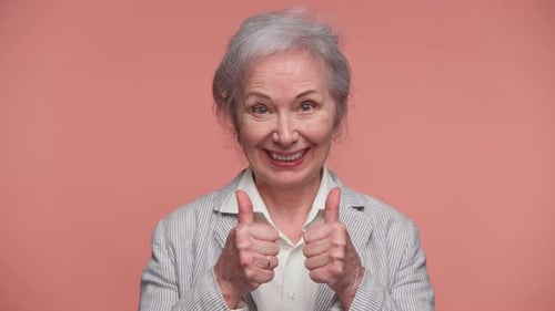 Smiling Senior Woman Giving Thumbs Up Gesture on Pink