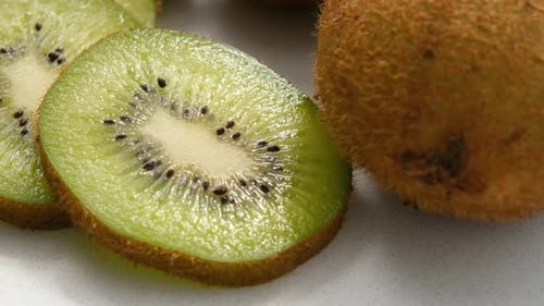 Nahaufnahme von ganzen und in Scheiben geschnittenen Kiwis, die sich auf einer Marmoroberfläche gegen den Uhrzeigersinn drehen