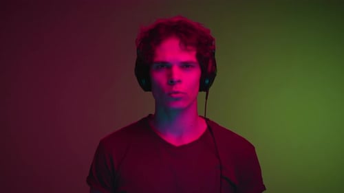 Portrait of Young Man in Headphones Listening Music in Neon Colors of Studio