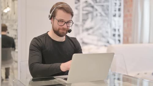 Young Adult Man with Headset Smiling at Camera in Call Center