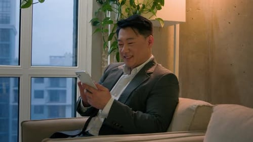 Man Smiling Using Smartphone in Modern Apartment