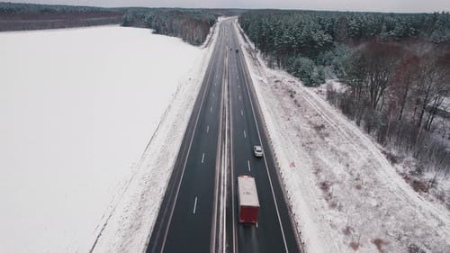 Luftbild der Bewegung von Autos auf der Autobahn zwischen schneebedeckten Feldern und Wäldern