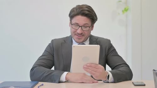 Video Call on Tablet by Middle Aged Businessman in Office