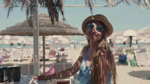 Attractive Happy Female Traveler with Sun Glasses and Straw Hat at the Beach Bar