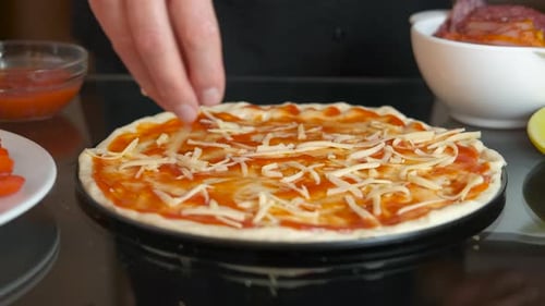 Una mujer espolvorea una masa de pizza con queso rallado