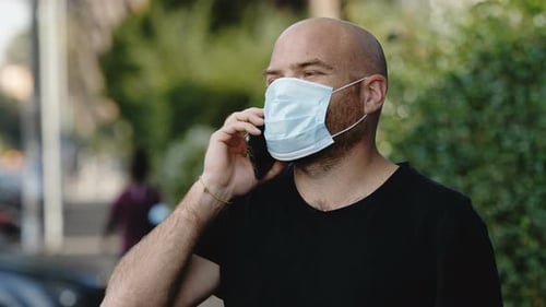 Kommunikation in Zeiten von Covid - junger Mann mit Maske spricht auf seinem Handy