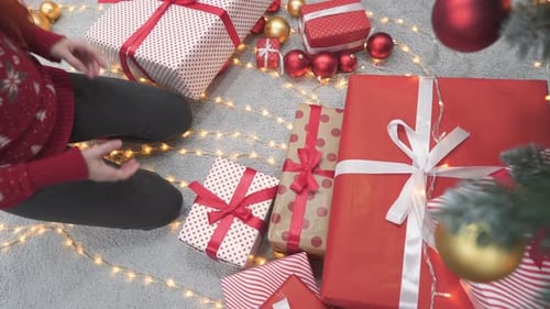 Woman Places Christmas Gifts Under Decorated Tree