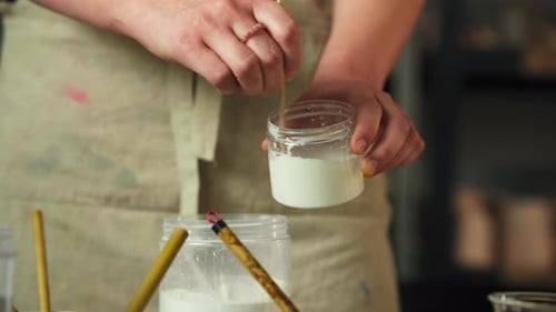 The Person Stirs a Glaze Mixture in a Small Jar, Preparing it For Clay Cup Glazing - Close Up