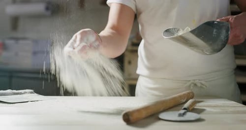 Baker Sprinkling Flour on Wooden Table in Kitchen