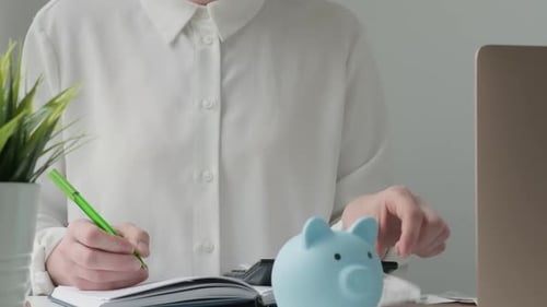 Woman Using Pen Writing on Bank Account Book Holding the Bills to Calculate at Home Workplace Table