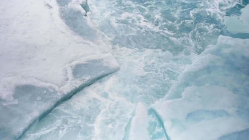 Luftaufnahme von zerbrochenem Meereis mit schwimmenden Eisschollen, gezackten Rissen und wirbelndem blaugrünen Schmelzwasser