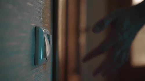 Mão estendida para ligar o interruptor de luz em um quarto escuro, iluminando o espaço e promovendo a sensação de calor