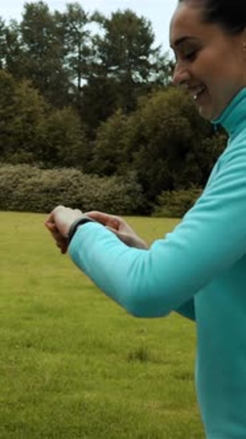 Woman Uses Smartwatch While Jogging Through Green Field