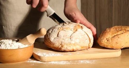 Person Cutting Fresh Baked Bread on Wooden Board