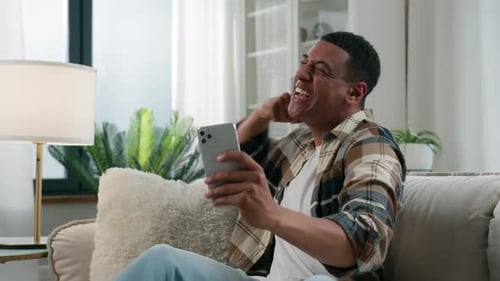 Man Celebrates Success on Mobile Phone at Home