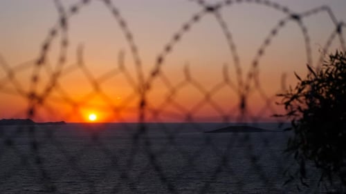 Sunset Over Ocean Seen Through Barbed Wire Fence