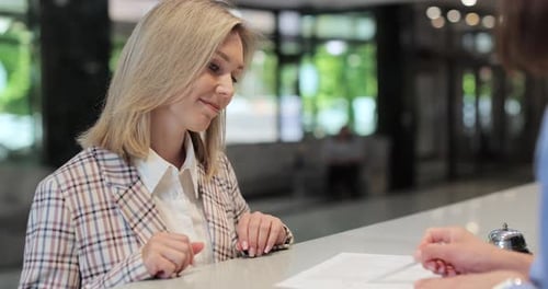 Woman Signs Document at Hotel Reception Desk