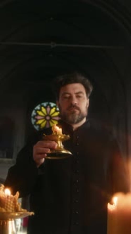 Vertical of Priest Placing Candle on Altar Praying in Dim Lit Church