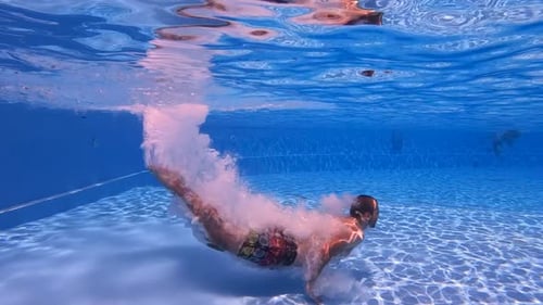 Man dives underwater in slow motion swimming pool