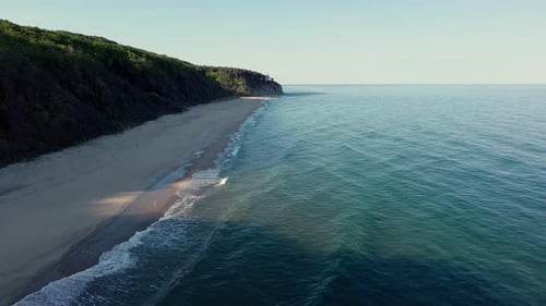 Beach Between a Ledge Covered with Vegetation and a Black Sea Under a Clear Blue Sky