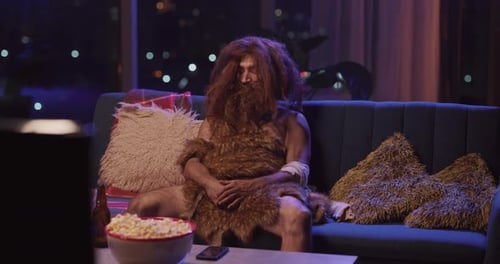 Primitive Human Ancestor in Animal Fur Sleeping While Sitting on Couch in Living Room Bearded Man
