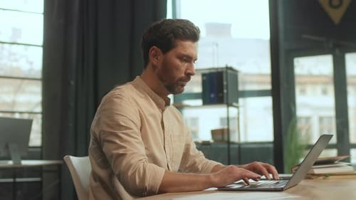 Attractive Worker Man Sitting at Desk Use Laptop Typing on Keyboard in the Office Serious
