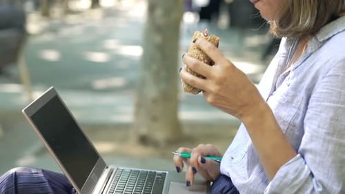 Junge Frau genießt Mittagspause, Sandwich und Laptop-Arbeit auf der Stadtbank
