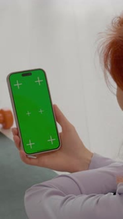 Vertical video Redhead woman swipes a smartphone with a green screen during gym break