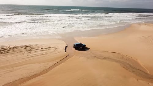 An offroad 4x4 vehicle driving along a beautiful sandy beach in Australia. Aerial view