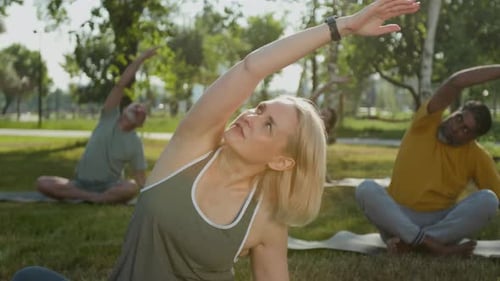 Female Sport Trainer Doing Side Bends with Seniors in Park in Summer