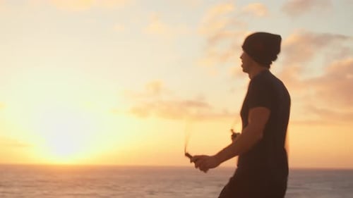 Sporty Man Exercising with Skipping Rope Overlooking Sea During Sunset